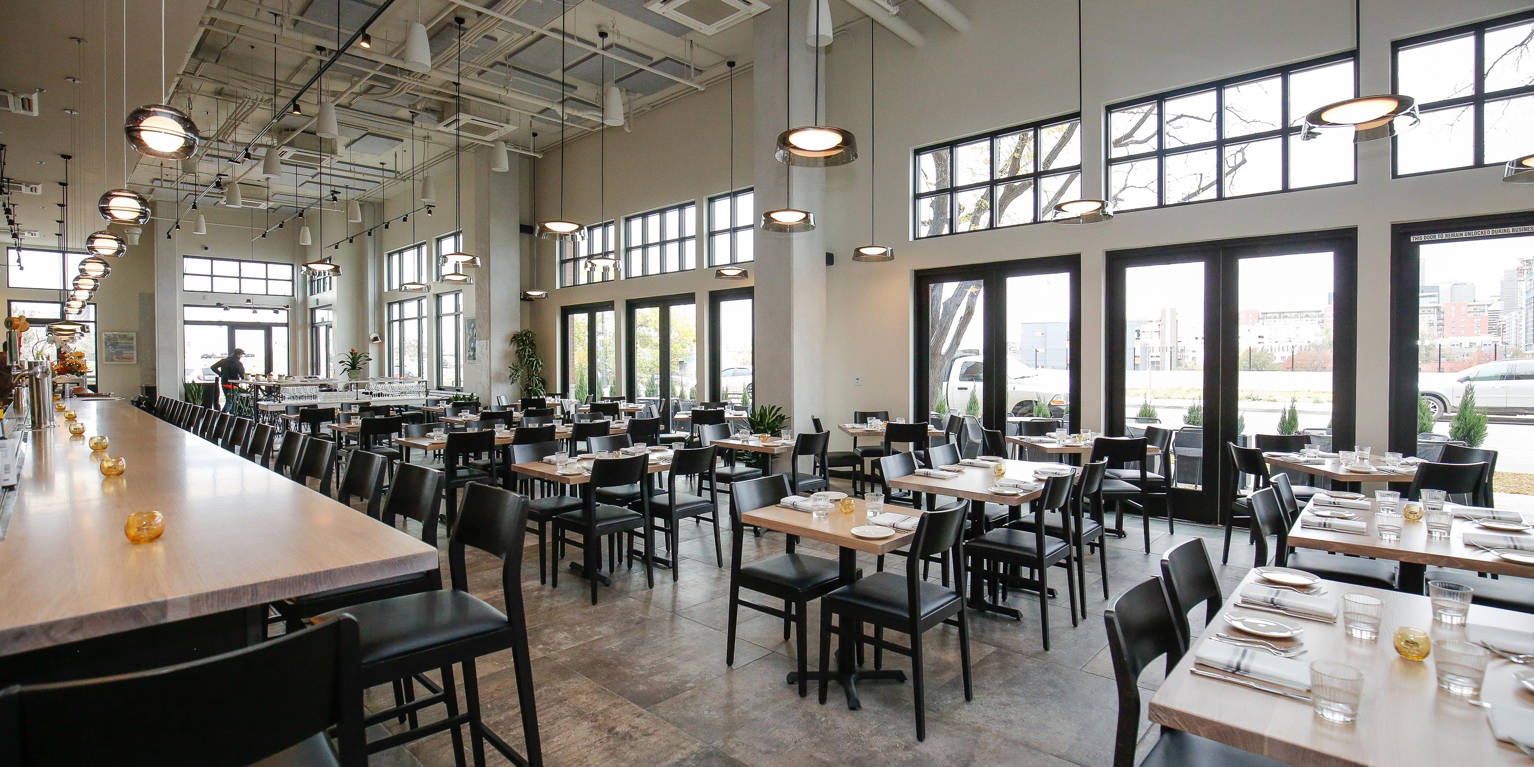 Contemporary restaurant with neatly arranged tables and a long bar counter in a bright setting.