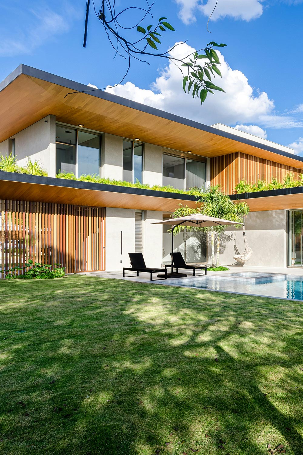 Modern two-story house with a lush green lawn, a swimming pool, and wooden accents.