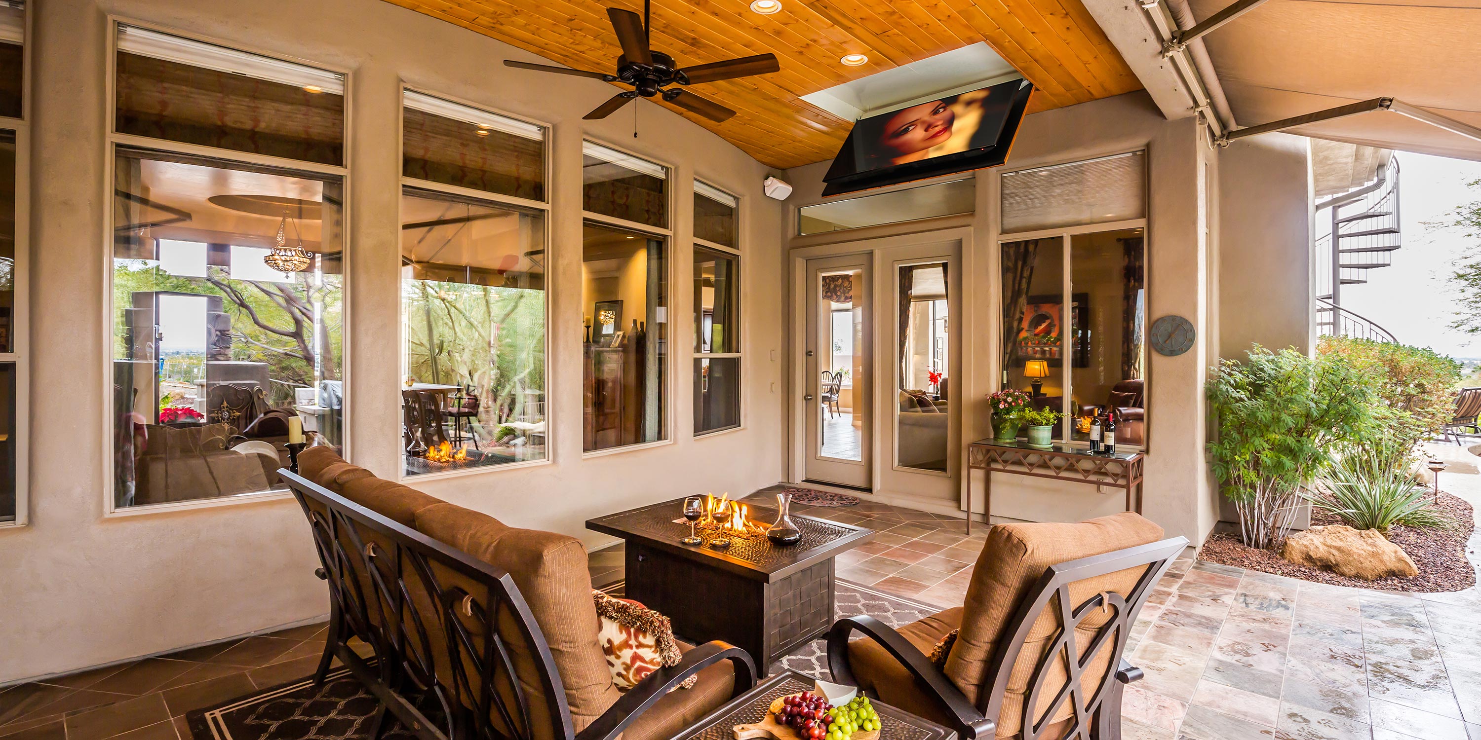 Covered outdoor patio with seating area, wall-mounted TV, and garden views.