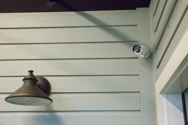 Outdoor security camera mounted on a wooden siding wall near a light fixture.