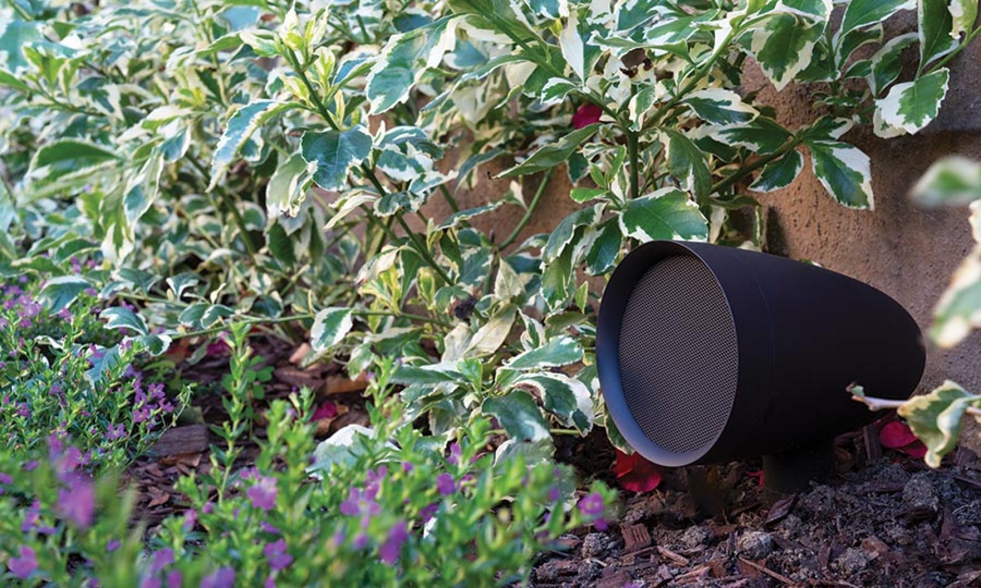 Outdoor speaker nestled among plants, blending into the garden landscape.