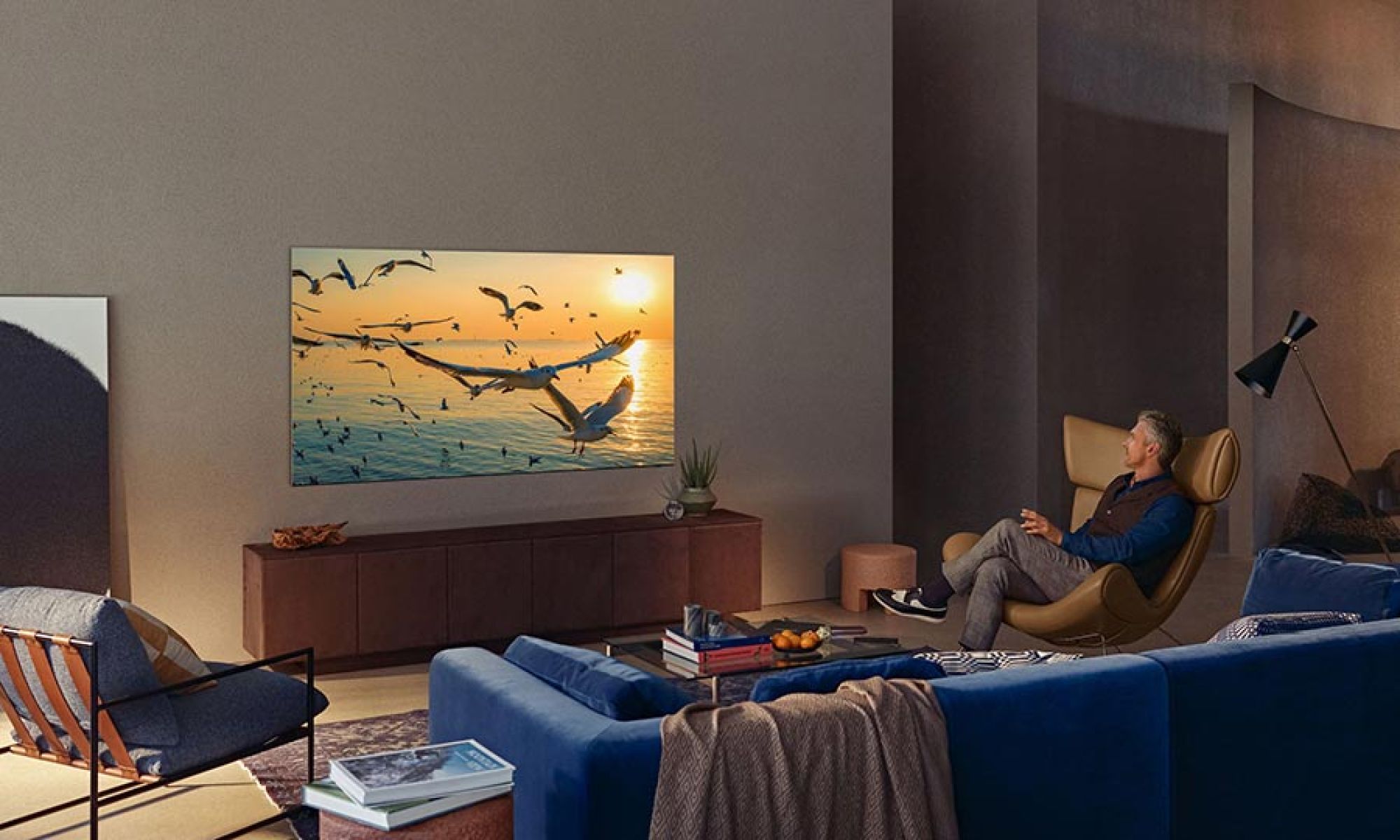 Person relaxing in a cozy living room watching a large TV mounted on the wall.