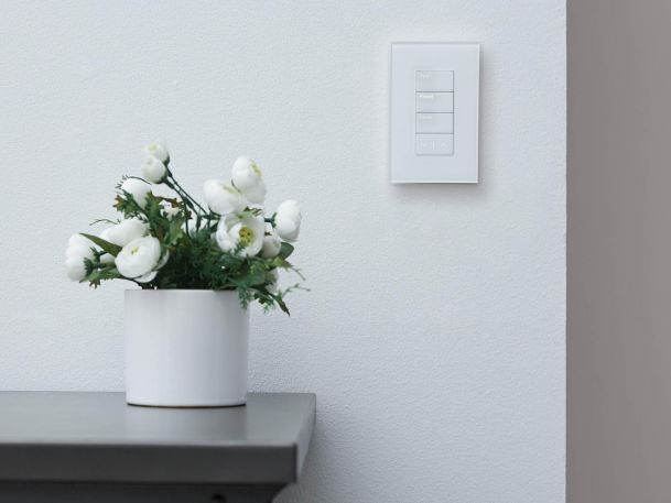White wall-mounted smart home control panel beside a vase of flowers.