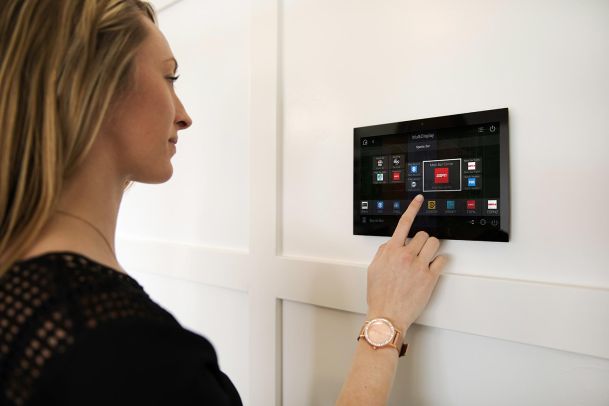 Woman interacting with a wall-mounted smart home control panel.