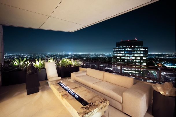 Luxurious rooftop lounge with a fire pit and panoramic city views at night.