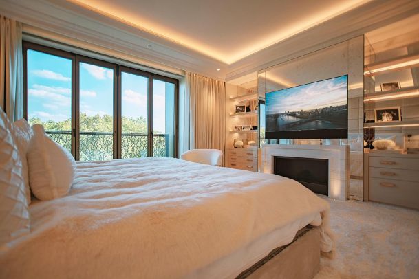 Cozy bedroom with a fireplace, large TV, and soft ambient lighting.