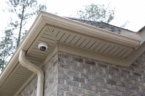 Dome security camera installed under the eaves of a brick house.