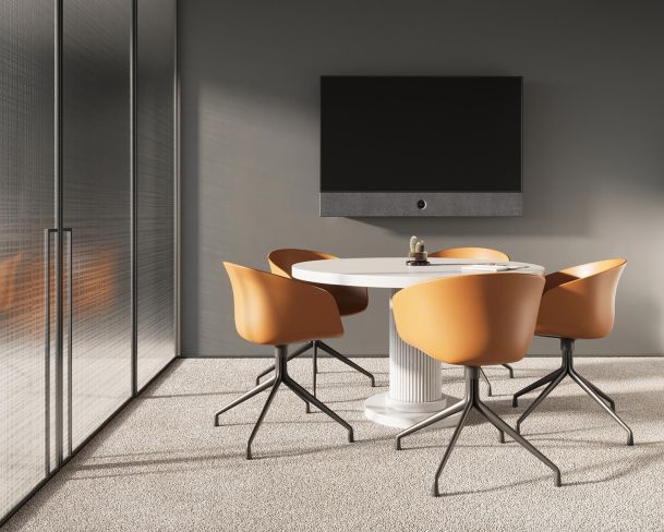 Minimalist meeting room with a round table, orange chairs, and a wall-mounted TV.